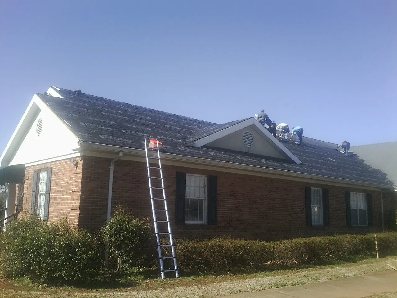 Crew tearing shingles off a brick ranch roof with a ladder set — Emergency Roof Repair work by our crew in Rio Vista