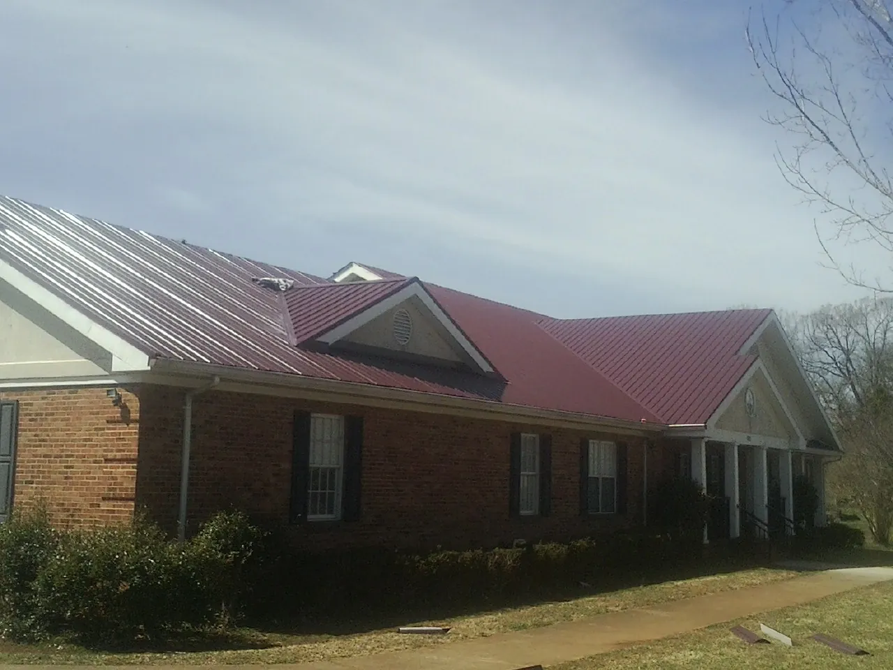 Red metal roof with gabled entries on a long brick building, from a Hail Damage Roof Repair job in Rio Vista